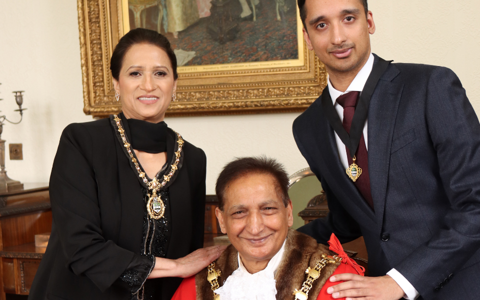 Left Mayoress, Hamida Begum wearing black dress and decorative chains, Mayor of Blackburn with Darwen, Councillor Mahfooz Hussain,centre, wearing red ceremonial cape and chains and son and Consort, Dr Adil Hussain wearing black suit and medal.